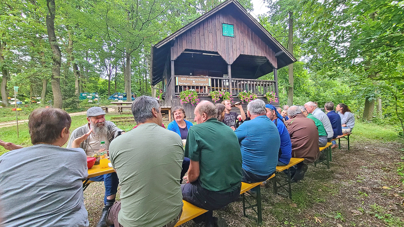 Menschen auf Heurigenbänken vor der Holzhütte im Schweizerstil